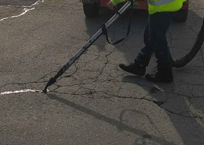 A man using a hose to clean a crack in the road.