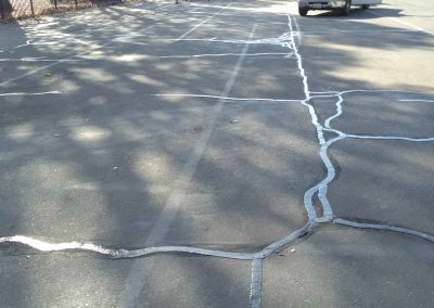 A car is parked in a parking lot with cracks in the pavement.