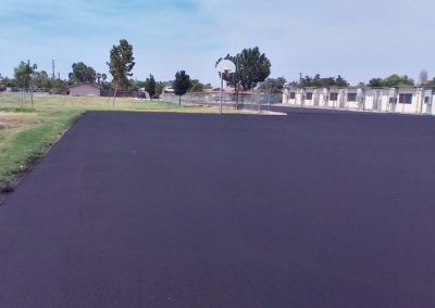 A black parking lot with a basketball court in the background.